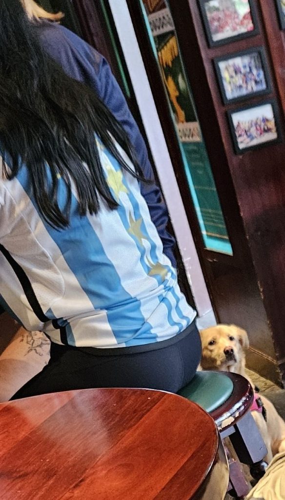 A sad looking dog next to a lady in an Argentinian rugby shirt, taken while Argentina were losing to New Zealand in the 2024 Rugby Championship.