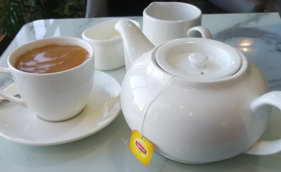 A white teapot, sugar bowl, milk bowl and cup of tea on a saucer.
